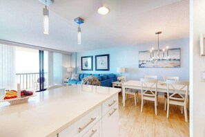 A modern kitchen with a central island, a dining area with white chairs, and a blue sofa. - Sea Colony Ocean 6th floor condo w/ basketball court, elevator, and free WiFi (Bethany Beach)