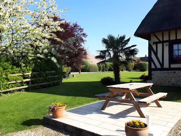 A picnic table with benches, a thatched-roof building, and a well-maintained lawn.