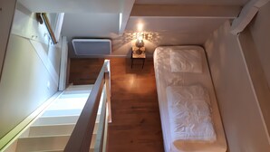 Habitación pequeña y funcional con una cama individual, una mesita de noche con lámpara y una ventana que deja entrar luz natural.