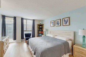 Une chambre à coucher comprenant un lit, une table de chevet, une commode, une chaise, une bibliothèque et une fenêtre avec des rideaux.