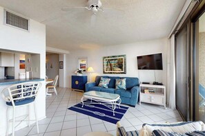 Ein modernes Wohnzimmer mit Sofa, Couchtisch und Fernseher. Es gibt eine Küchenzeile mit Bar und Stühlen.