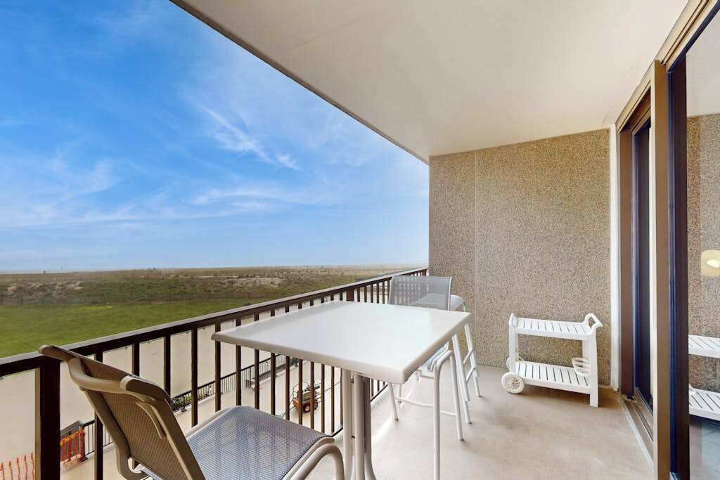 Ein Balkon mit Tisch und Stühlen, einer kleinen weißen Ablagefläche und Blick auf die Landschaft.