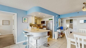 Una cocina moderna con una isla central, taburetes de bar y una zona de comedor con mesa y sillas.