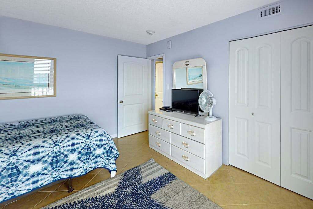 A bedroom with a bed, dresser, TV, and a door.