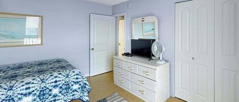 A bedroom with a bed, dresser, TV, and a door.
