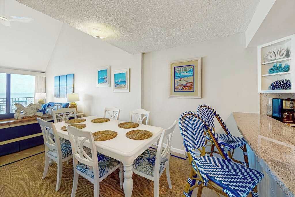 A dining area with a white table, blue and white patterned chairs, and a beach-themed wall art.