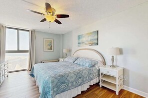 A bedroom with a bed, bedside tables, a ceiling fan, and a window with curtains. - Sea Colony oceanfront condo with pool, hot tub, sauna, basketball, elevator (Bethany Beach)