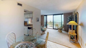 Sala de estar com área de jantar, varanda com vista e cozinha ao fundo.