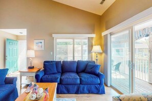 Ein Wohnzimmer mit einem blauen Sofa, einem Holztisch und Blick durch eine Glastür auf eine Terrasse.