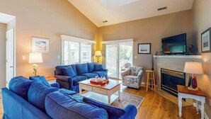 A living room with a sofa set, a television, a fireplace, and a large window. - Sea Colony Tennis 2nd-floor condo with basketball court, pool, & tennis court (Bethany Beach)