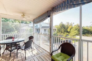 Ein überdachter Außenbereich mit Tisch und Stühlen, einem Deckenventilator und Blick auf die Nachbarschaft.