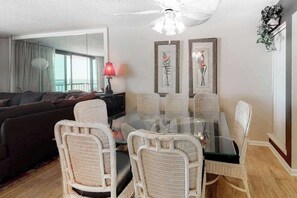 Ein Wohnzimmer mit einem Esstisch aus Glas, umgeben von Korbstühlen, einem Sofa und einem Deckenventilator.
