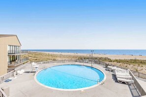 Una piscina amb vistes a la platja, gandules i un edifici amb balcons.