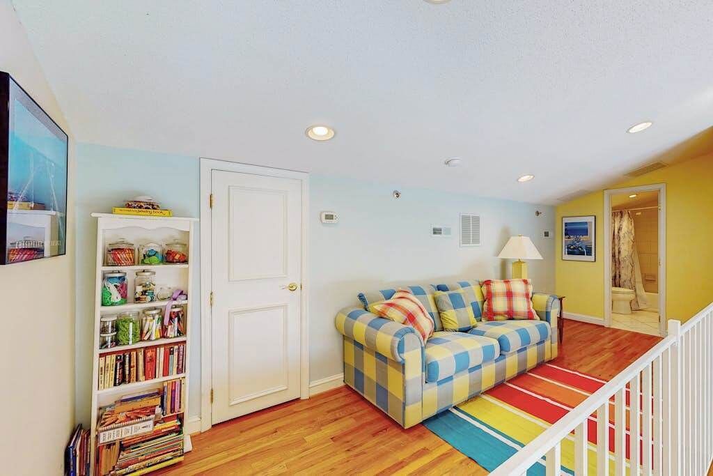 A living room with a checkered sofa, a bookshelf, and a staircase.