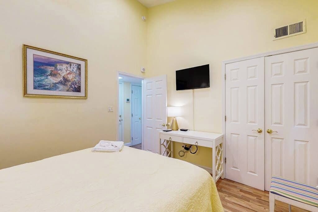 A bedroom with a bed, a desk with a lamp, a TV, and a wardrobe.