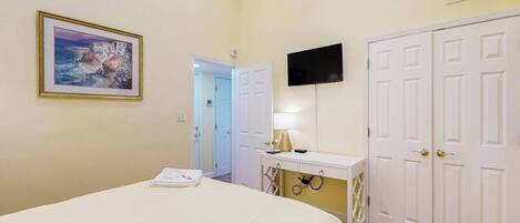 A bedroom with a bed, a desk with a lamp, a TV, and a wardrobe.