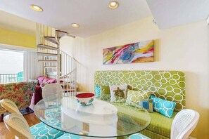 A modern living room with a glass coffee table, a green patterned sofa, a colorful abstract painting, and a spiral staircase. - Sea Colony Ocean 9th floor condo w/ elevator, basketball court, and free WiFi (Bethany Beach)