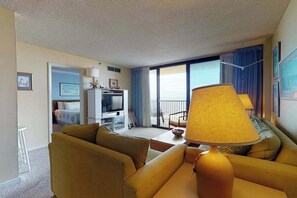 A hotel room with a sofa, a lamp, a television, a balcony with a view, and a dining area. - Sea Colony Ocean 7th floor condo w/ free WiFi, elevator, and tennis court (Bethany Beach)