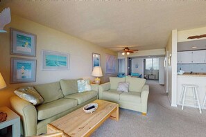 A living room with two sofas, a coffee table, and a kitchen area with cabinets and a bar stool. - Sea Colony Ocean 7th floor condo w/ free WiFi, elevator, and tennis court (Bethany Beach)
