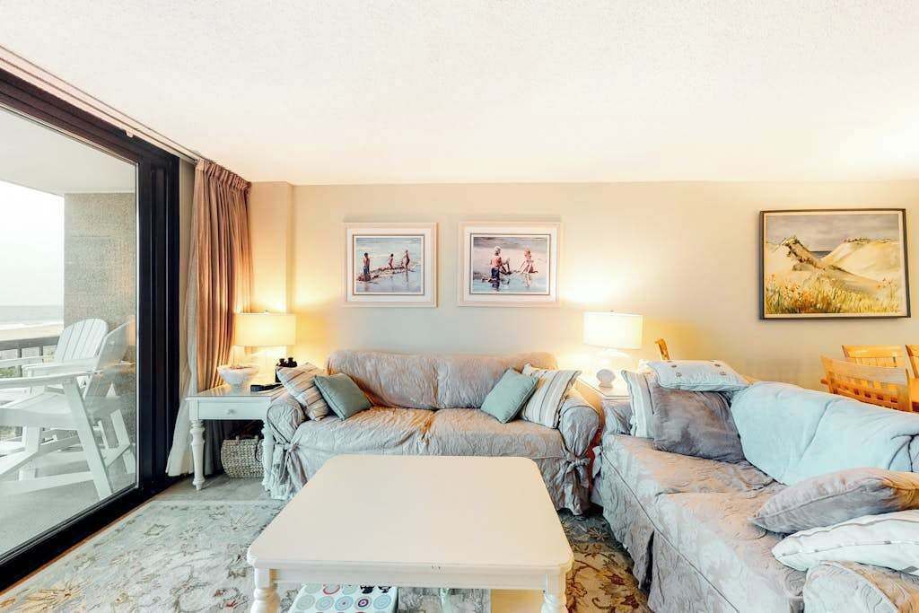 A hotel room with a sofa, a small table, two lamps, and artwork on the walls.