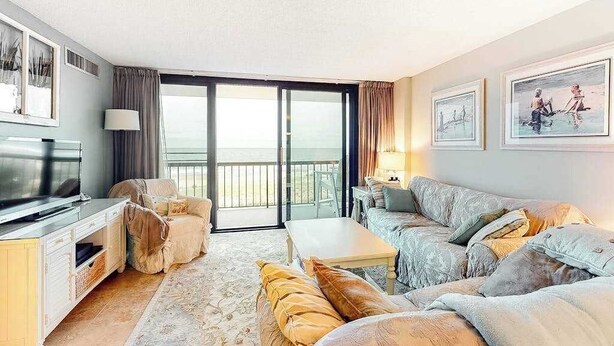 A living room with a sofa, a coffee table, a TV, and a balcony with a view. - Sea Colony Ocean 3rd-floor condo with elevator & gym (Bethany Beach)