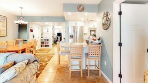 A modern kitchen with a refrigerator, dining table, and chairs. There is a clock on the wall and a door on the right. - Sea Colony Ocean 3rd-floor condo with elevator & gym (Bethany Beach)