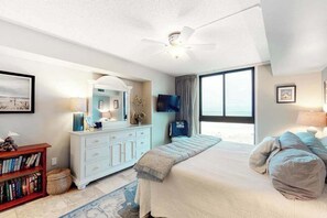 Ein Schlafzimmer mit einem Bett, einem Schminktisch, einem Fernseher und einem großen Fenster.