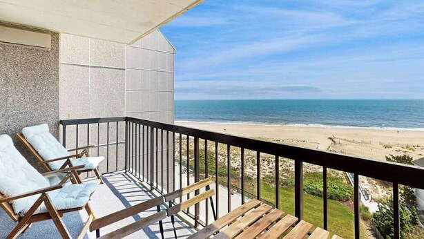 A balcony with a view of the beach, two lounge chairs, and a wooden bench. - Sea Colony Ocean 7th floor condo w/ basketball court, pool, and elevator (Bethany Beach)