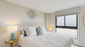 Ein Schlafzimmer mit einem Bett, zwei Nachttischlampen, einer Wanddekoration und einem großen Fenster.