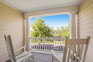 A porch with two white chairs, a railing, and a view of a parking lot and trees. - Bayside Resort townhouse with golf on-site, pool access, fireplace, & central AC (Selbyville)