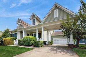 A residential house with a covered porch, a garage, and a well-maintained lawn. - Bayside Resort house with pool, lakefront, golf on-site, & tennis court (Selbyville)