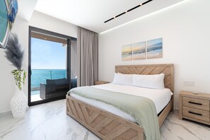 Een moderne slaapkamer met een groot bed, uitzicht op zee, een kamerplant en een nachtkastje.