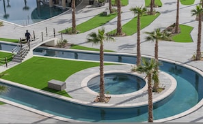 A pool area with palm trees, a circular water feature, and a staircase leading to a building. - Beachfront 2BR Condo Pool Ocean Views Resort (Puerto Peñasco)