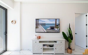 Un tavolo consolle bianco con cassetti, una TV a parete che mostra vista sulla piscina, una pianta in vaso e una porta sulla destra.