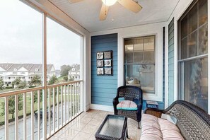A balcony with a view of houses, a ceiling fan, and a blue wall with framed pictures. - Bayside Resort 4th floor condo w/ gym, tennis court, and free WiFi (Selbyville)