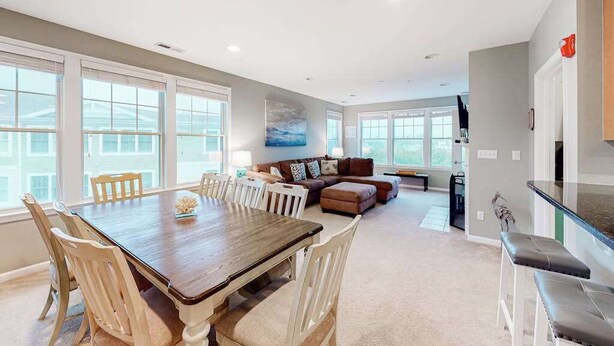 A spacious living area with a dining table, chairs, a sofa, and a kitchen area. - Bayside Resort 4th floor condo w/ gym, tennis court, and free WiFi (Selbyville)