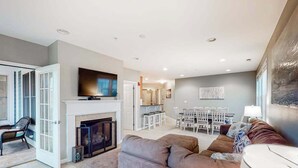 A modern living room with a fireplace, a television, and a dining area with a table and chairs. - Bayside Resort 4th floor condo w/ gym, tennis court, and free WiFi (Selbyville)