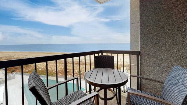 Un balcon avec une table et des chaises, donnant sur une plage et une piscine.