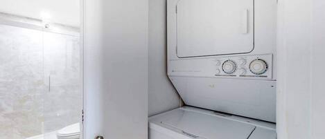 Ett litet och praktiskt tvättrum med tvättmaskin och torktumlare, en kaklad duschhörna och en vit dörr.