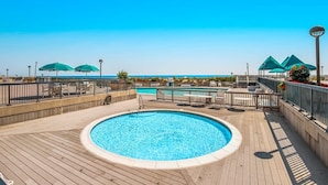 Un espace piscine doté d’une terrasse en bois, de chaises longues et de parasols.