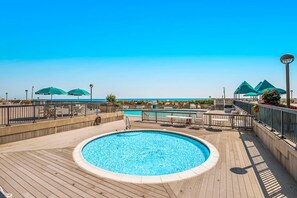 A pool area with a wooden deck, lounge chairs, and umbrellas. - Sea Colony Ocean 6th floor condo w/ tennis court, balcony, and shared sauna (Bethany Beach)