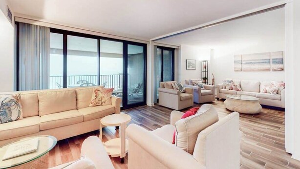 Ein geräumiges Wohnzimmer mit einer Couch, Sesseln, einem Couchtisch und einem Balkon mit großen Fenstern.