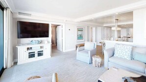 Een ruime woonkamer met een flatscreen televisie, witte meubels en een eethoek.