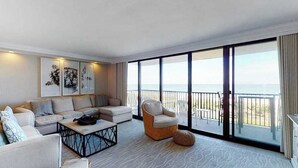 Een moderne woonkamer met een bank, fauteuils, een salontafel en een groot raam met uitzicht op zee.
