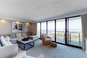 Un salon moderne comprenant un canapé, des fauteuils, une table basse et une grande fenêtre donnant sur la mer.