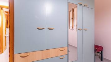A wardrobe with multiple drawers and doors, a mirror, and a small chair with a red cloth.