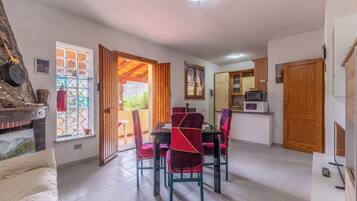 A dining area with a table and chairs, a kitchen with appliances, and a view through an open door.
