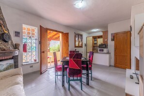 A dining area with a table and chairs, a kitchen with appliances, and a view through an open door. - Appartamento Posada (Posada)
