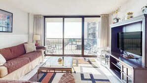 Un salon comprenant un canapé, une table basse, un téléviseur et un balcon aménagé avec du mobilier d’extérieur.