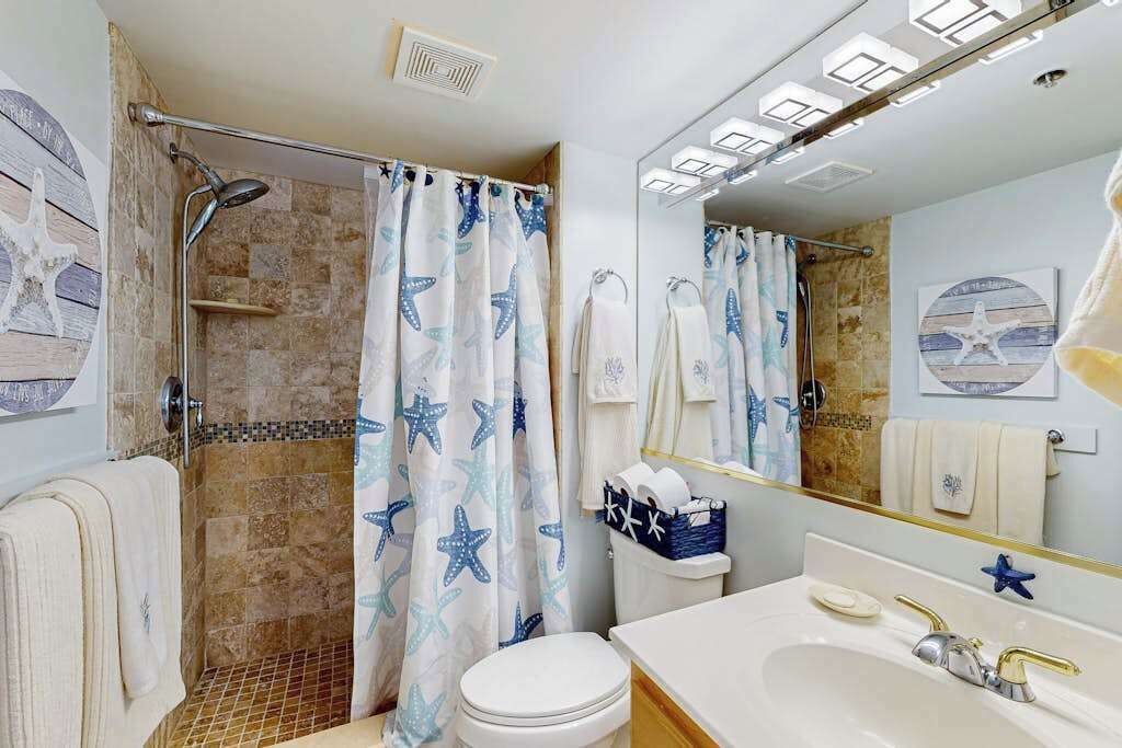 Ein Badezimmer mit Dusche, Toilette, Waschbecken und einem großen Spiegel.